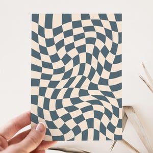 May include: A card with a wavy checkerboard pattern. The design features alternating squares of a muted teal color and a cream color. The card is held by a hand, and the background is a neutral white.