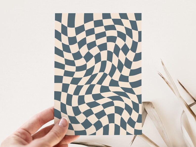 May include: A card with a wavy checkerboard pattern. The design features alternating squares of a muted teal color and a cream color. The card is held by a hand, and the background is a neutral white.