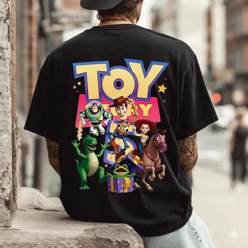 Puede incluir: Una camiseta negra con un gr&aacute;fico grande en la espalda con el texto TOY STORY. El dise&ntilde;o incluye ilustraciones coloridas de Buzz Lightyear, Woody, Jessie, Bullseye, Rex y un alien&iacute;gena verde saliendo de una caja de regalo morada.