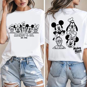 May include: White t-shirt featuring a black and white graphic of Mickey Mouse and friends. The front of the shirt displays the text "Mickey & Co. Est. 1928" above the characters. The back of the shirt has Mickey Mouse, Goofy, Donald Duck, and Minnie Mouse.