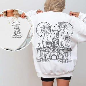 Op de afbeelding: Witte sweatshirt met een zwart-wit illustratie van Mickey Mouse op de voorkant en een kasteel met vuurwerk op de achterkant. Het ontwerp bevat Mickey Mouse oren en sterren.