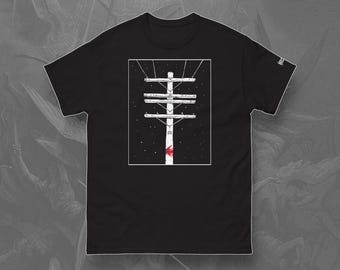May include: Black t-shirt featuring a white and black illustration of a utility pole with wires against a starry background. The design includes a red accent at the base of the pole. The word "FRONT" is printed at the bottom of the shirt.