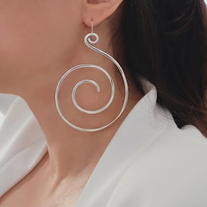 May include: Silver spiral earrings. These large, dangling earrings feature a continuous spiral design. The earrings are made of a shiny, silver-coloured metal and hang from a simple hook.