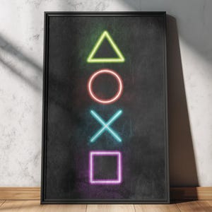 Könnte beinhalten: Ein gerahmtes Poster mit Neon-PlayStation-Controller-Symbolen: ein grünes Dreieck, ein roter Kreis, ein blaues X und ein lila Quadrat. Die Symbole sind vertikal auf einem schwarzen Hintergrund angeordnet. Das Poster steht vor einer strukturierten weißen Wand.