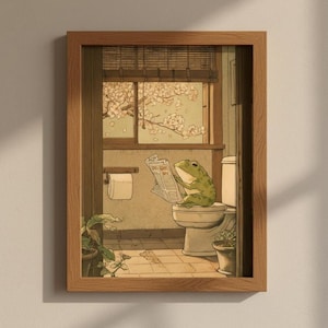 Op de afbeelding: Een ingelijste kunstdruk met een groene kikker die een krant leest op een toilet. De badkamer heeft een raam met uitzicht op bloeiende bomen, een toiletpapierrol en potplanten. De lijst is van hout.