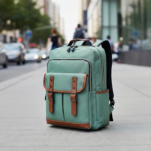May include: A green backpack with brown leather accents. The backpack has a rectangular shape with a top handle, front flap pockets, and adjustable shoulder straps. The bag is made of a durable material and is suitable for everyday use.