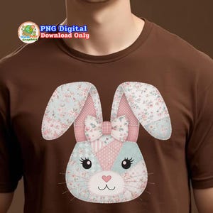 以下が含まれることがあります： 茶色のTシャツ。パッチワークのウサギのデザイン。ウサギはピンクと青の花柄、ピンクのリボン、ハート型の鼻をしています。Tシャツのテキストは「PNG Digital Download Only」です。