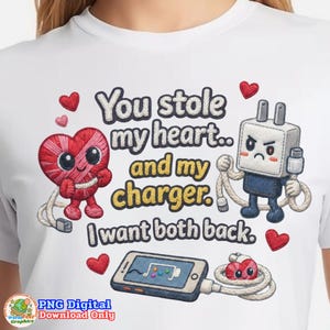 May include: White t-shirt featuring a cartoon design with the text "You stole my heart.. and my charger. I want both back." The design includes a heart character, a charger character, a smartphone, and hearts.