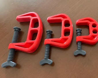 May include: Four red C-clamps of different sizes, lined up. Each clamp features a grey screw mechanism for adjusting the opening. The clamps are made of a solid material and are designed for clamping in woodworking or other tasks.