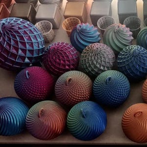 May include: A display of vibrantly coloured, spherical decorative items with complex geometric designs. The spheres come in various sizes and colours, including blue, orange, red, and white. Some have a spiral pattern, while others feature a lattice or textured surface. The items are arranged on a neutral surface.