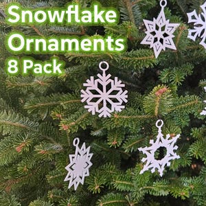 May include: White snowflake ornaments hanging on a green Christmas tree. The image shows eight different snowflake designs. Text in the upper left corner reads "Snowflake Ornaments 8 Pack."