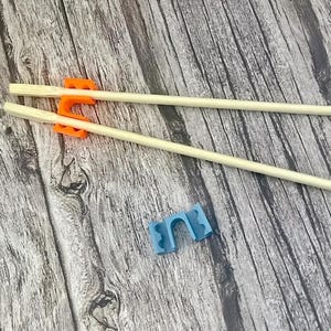 以下が含まれることがあります： 木製の箸とオレンジ色の箸置き、青色の箸置きが木製の表面に置かれています。箸は明るい色で、箸置きはプラスチック製です。