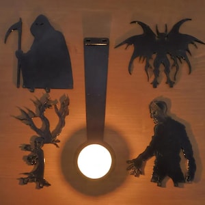 May include: Black metal Halloween decorations including a Grim Reaper with a scythe, a bat-like creature, a zombie, and a spooky tree. The decorations are arranged around a central light source, creating a dramatic effect.