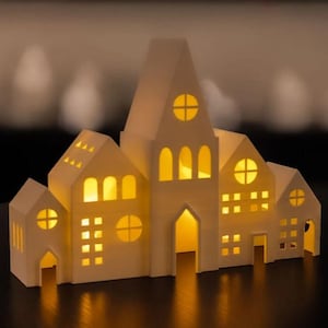 Pode incluir: Uma casa decorativa branca de vários edifícios com janelas e portas iluminadas. A casa apresenta uma torre central alta e várias estruturas menores, todas com janelas recortadas. A iluminação interior quente cria um ambiente acolhedor e convidativo. É um artigo decorativo.