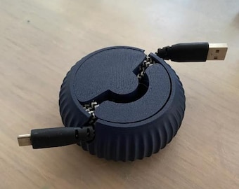 May include: A dark blue, round cable organizer with a zipper-like design. The organizer has a ribbed exterior and holds a USB cable and a USB-C cable. The cables extend from the sides of the organizer, ready for use.