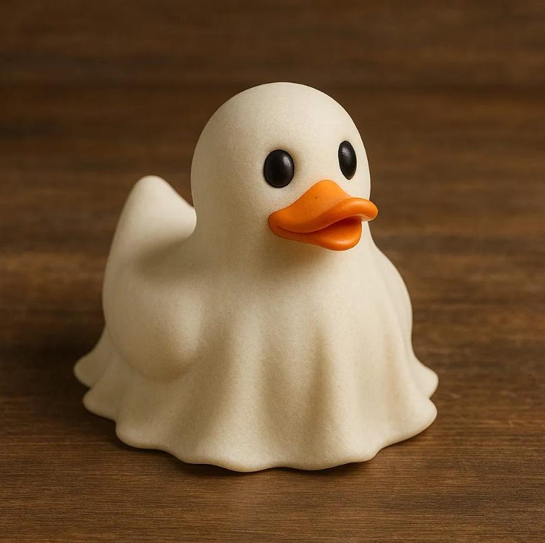 May include: A whimsical, off-white rubber ducky shaped like a ghost. It has black eyes and an orange beak. The duck is sitting on a wooden surface.