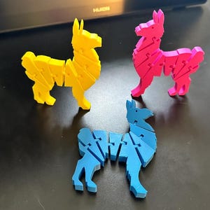 Puede incluir: Tres rompecabezas de llama coloridos en amarillo, rosa y azul. Cada llama está construida con piezas entrelazadas, mostrando un diseño lúdico. Los rompecabezas están sobre un fondo oscuro, resaltando sus colores vibrantes y su construcción única.