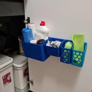May include: A blue plastic organizer with multiple compartments is mounted on a white cabinet door. The organizer holds cleaning supplies, including a bottle of detergent, a roll of paper towels, and sponges.