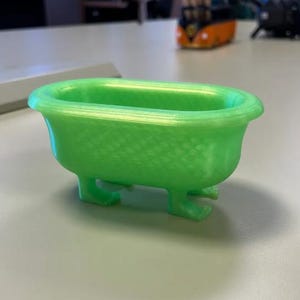 May include: A small, bright green bathtub with four curved feet. The miniature tub has a textured surface and a classic, rounded shape. This decorative item could be used as a unique container or display piece.