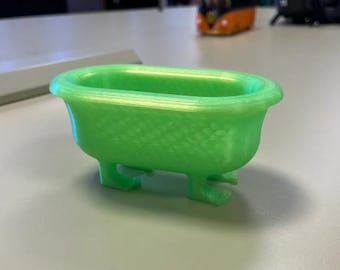 May include: A small, bright green bathtub with four curved feet. The miniature tub has a textured surface and a classic, rounded shape. This decorative item could be used as a unique container or display piece.