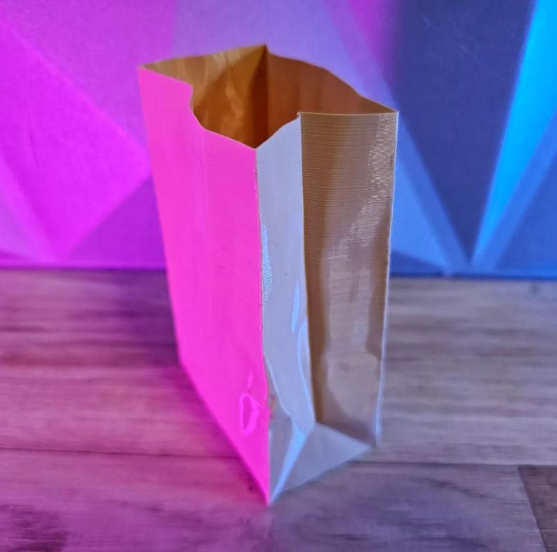 May include: A paper bag with a neon pink front panel and a natural brown interior. The bag is open at the top, revealing the interior. The background is a gradient of pink, blue, and purple.