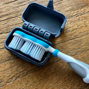 May include: A blue and white toothbrush with a matching travel case. The toothbrush has a blue head and white bristles. The case is dark blue and has a hinged lid. The handle is white and gray.