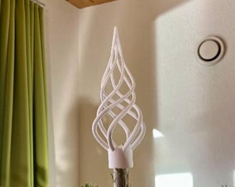 May include: A white, decorative tree topper with a spiral design. The topper is made of intertwined, curved lines that form a conical shape. The base is a white cylinder, and the topper is placed on a tree branch.