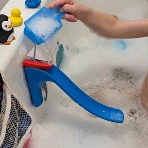 Op de afbeelding: Een blauw waterspeelgoed met een rode boot en een wit zeil wordt gebruikt in een badkuip vol bellen. Andere badspeeltjes zijn een blauwe walvis, een gele eend en een pinguïn.