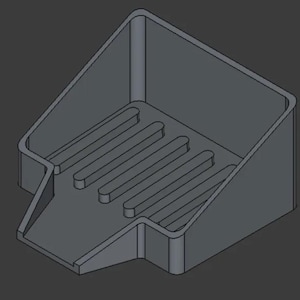 May include: A gray, 3D-rendered soap dish with a rectangular base and a sloped front. The dish features a series of parallel grooves for drainage and a raised back and sides. The design is simple and functional.