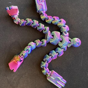 May include: A flexible, articulated toy in a rainbow color scheme. The toy is composed of connected segments, forming a shape with hand-like and head-like ends. The color transitions from pink to blue and green.