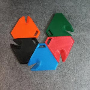 May include: A collection of six colorful, geometric shapes in orange, green, red, black, and blue. Each shape has a unique cutout and a small handle. The objects are arranged in a circular pattern on a gray surface.