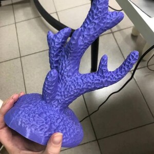 May include: A vibrant purple coral sculpture with a textured surface. The coral has multiple branches extending upwards from a rounded base. The sculpture is held in a person's hand, showcasing its size and detail. The piece is likely a decorative item.