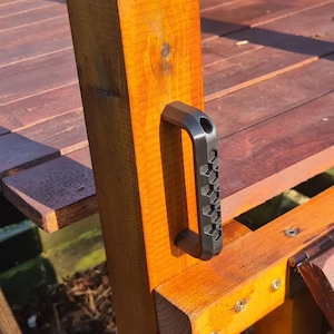 May include: A wooden playset with a dark metal handle. The playset is made of stained wood and has a platform and a ladder. The handle is black and has a textured grip. The playset is made of wood.