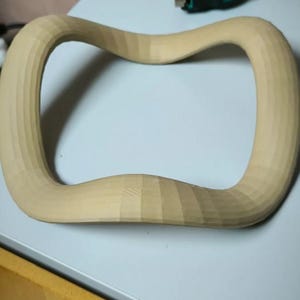 May include: A light-colored, wooden, curved object with a rectangular shape and rounded corners. The wood has a natural, unfinished appearance, with visible grain and a textured surface. The object appears to be hand-carved.