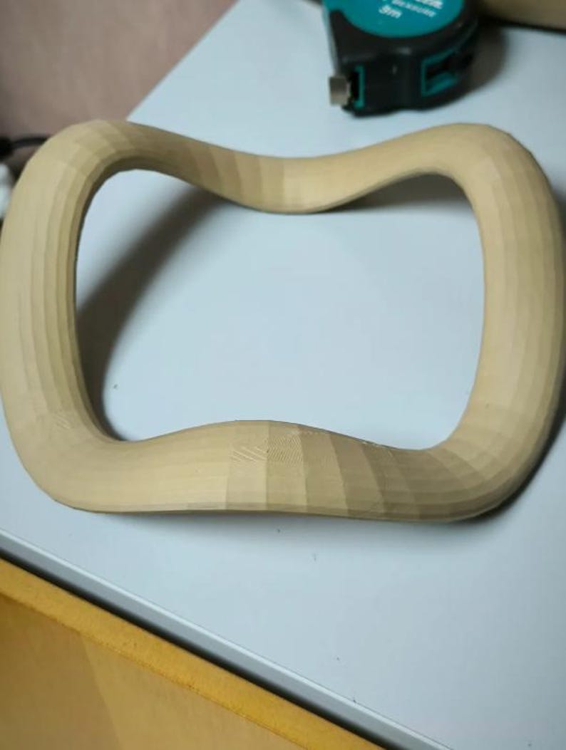 May include: A light-colored, wooden, curved object with a rectangular shape and rounded corners. The wood has a natural, unfinished appearance, with visible grain and a textured surface. The object appears to be hand-carved.