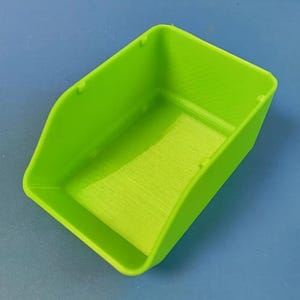 Peut inclure: Un récipient rectangulaire vert vif avec un devant incurvé et un intérieur texturé. Le récipient est en plastique et repose sur une surface bleue. Le récipient a un petit rebord sur le bord supérieur.