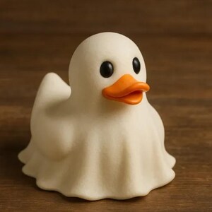 May include: A whimsical white duck figurine with a ghost-like drape. The duck has black eyes and an orange beak. The figurine is set against a brown wooden background. This decorative item is perfect for Halloween or a quirky home decor.
