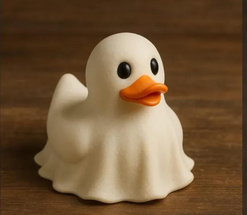 May include: A whimsical white duck figurine with a ghost-like drape. The duck has black eyes and an orange beak. The figurine is set against a brown wooden background. This decorative item is perfect for Halloween or a quirky home decor.
