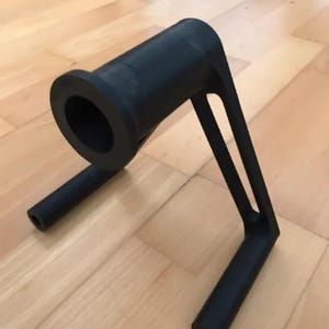 Puede incluir: Objeto negro impreso en 3D con un ca&ntilde;&oacute;n cil&iacute;ndrico y dos brazos de soporte. El ca&ntilde;&oacute;n tiene una abertura circular. Los brazos se extienden hacia abajo, terminando en soportes cil&iacute;ndricos. El objeto est&aacute; dise&ntilde;ado para un prop&oacute;sito espec&iacute;fico.