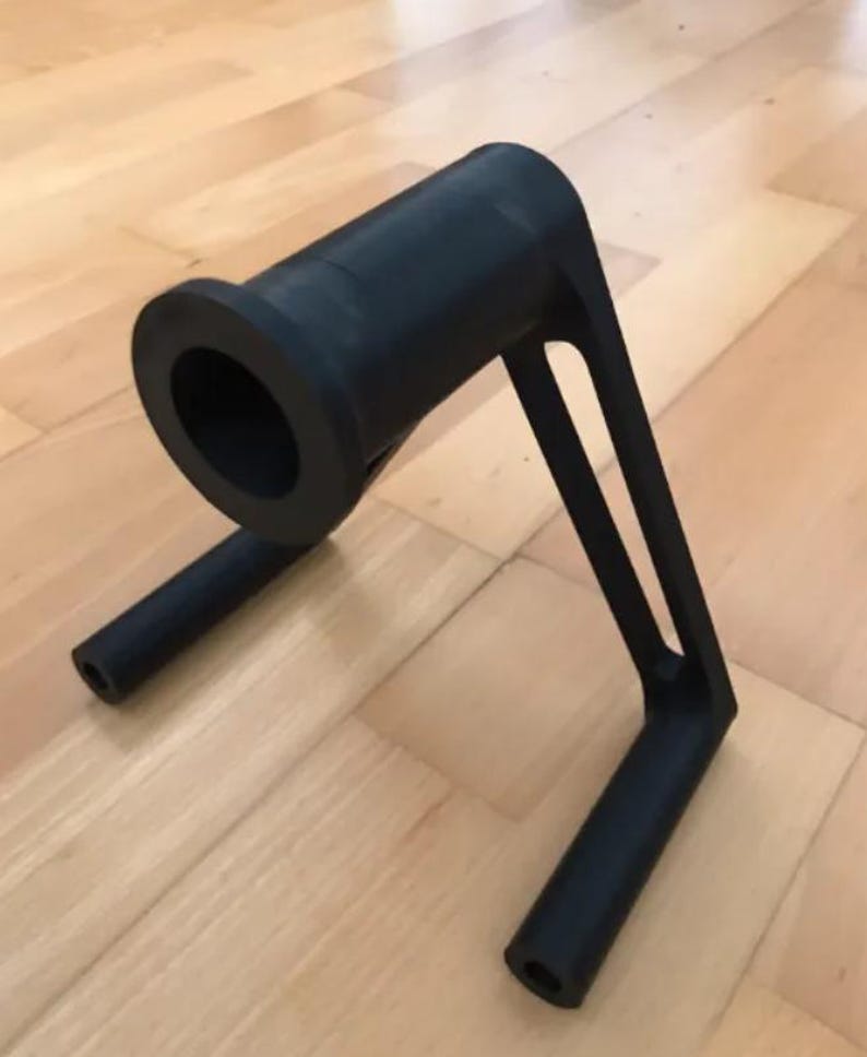 Puede incluir: Objeto negro impreso en 3D con un ca&ntilde;&oacute;n cil&iacute;ndrico y dos brazos de soporte. El ca&ntilde;&oacute;n tiene una abertura circular. Los brazos se extienden hacia abajo, terminando en soportes cil&iacute;ndricos. El objeto est&aacute; dise&ntilde;ado para un prop&oacute;sito espec&iacute;fico.