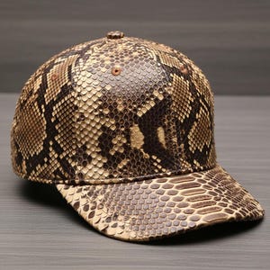 May include: A baseball cap with a snakeskin pattern in shades of brown and tan. The cap features a curved brim and a button on top. The snakeskin design covers the entire cap, creating a unique and textured appearance.