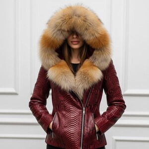 Puede incluir: Chaqueta de cuero burdeos con estampado de piel de serpiente, con una gran capucha y cuello adornado con piel de color canela. La chaqueta tiene cremallera plateada y bolsillos.