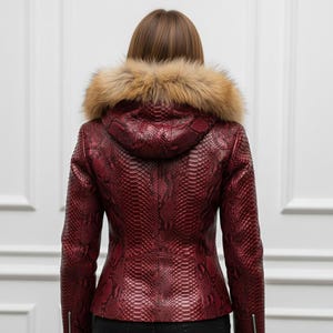 Puede incluir: Chaqueta de cuero burdeos con estampado de piel de serpiente, con capucha forrada de piel. La chaqueta tiene una silueta entallada, cierre de cremallera y un aspecto texturizado. El ribete de piel es de color marr&oacute;n claro.