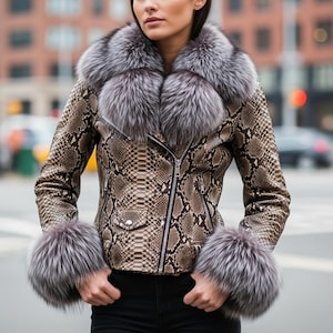 Pode incluir: Casaco de couro castanho e bege com padrão de pele de cobra, com gola e punhos de pele prateada. O casaco tem fecho de correr e um pequeno bolso no peito. A modelo usa calças pretas.