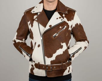 May include: A brown and white cowhide leather jacket with a classic asymmetrical zipper design. The jacket features a notched collar, zippered pockets, and a belt at the waist. The jacket is a statement piece.