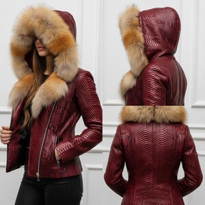 Puede incluir: Chaqueta de cuero burdeos con estampado de piel de serpiente, cierre de cremallera y capucha con ribete de piel marr&oacute;n. La chaqueta tiene una silueta entallada y un bolsillo delantero.
