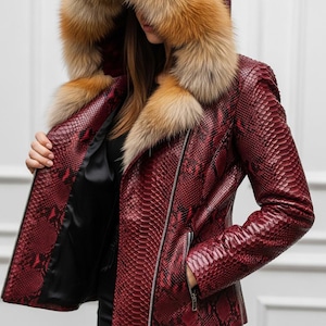 Puede incluir: Chaqueta de cuero roja con estampado de piel de serpiente y capucha con ribete de piel. La chaqueta tiene cierre de cremallera y forro negro. El ribete de piel es una mezcla de colores marr&oacute;n y beige. Prenda de abrigo elegante.