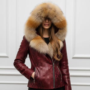 Puede incluir: Chaqueta de cuero burdeos con estampado de piel de serpiente, con una gran capucha y cuello forrados de piel. La chaqueta tiene cierre de cremallera y un bolsillo en el lado izquierdo. La piel es una mezcla de marr&oacute;n y beige.