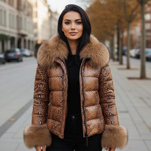 May include: A brown and tan snakeskin-patterned puffer jacket with a fur collar and cuffs. The jacket is zipped up and worn over a black top and black trousers. The background is a city street.