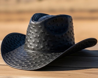 May include: A black cowboy hat with a textured surface and a wide brim. The hat is made of a dark material and sits on a wooden surface. The hat has a classic western design.